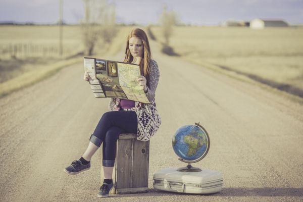 Imagem de uma mulher sentada no meio de uma estrada, olhando um mapa, com um globo terrestre e sua mala ao lado, representando o arquétipo do explorador.